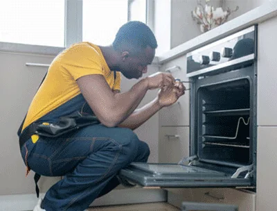 Technician kneeling at a built-in oven and fixing the door