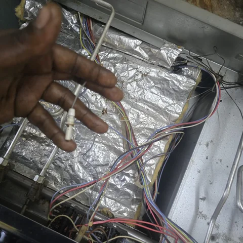 Technician holding a thermal fuse inside an oven with the wiring exposed