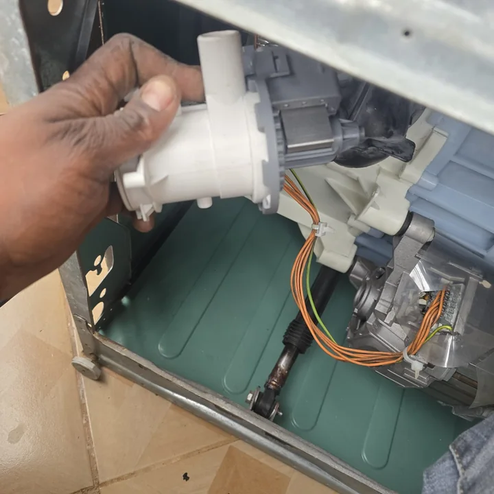 Technician removing the drain pump from underneath a washing machine